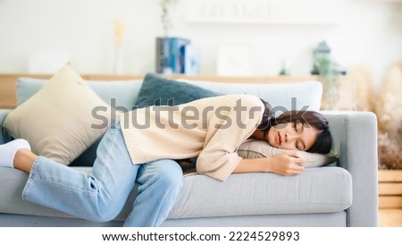 Asian woman resting at home on couch, feeling exhausted after work, lacking energy, or overworked, too tired, and lacking motivation Royalty-Free Stock Photo #2224529893
