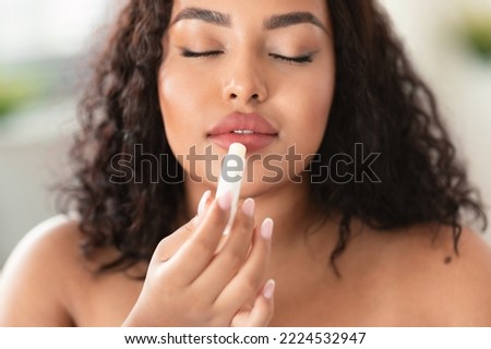 Young african american chubby lady applying lip balm, moisturizing and caring for skin, closeup shot. Beautiful black woman using cosmetic product, taking care of her lips Royalty-Free Stock Photo #2224532947