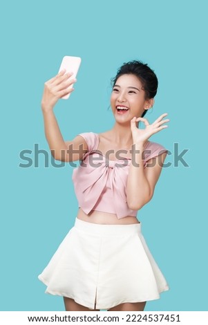 Image of emotional positive young pretty woman posing isolated over blue wall background take selfie by mobile phone showing peace gesture.
