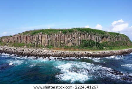 Beautiful coastal basalt columns of Tongpan Island under blue sunny sky, with a hiking path running under the cliffs and furious waves beating the off shore rocks, in Magong, Penghu County, Taiwan Royalty-Free Stock Photo #2224541267