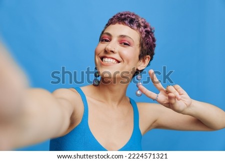 Young sports woman fashion blogger takes a picture of herself on the phone in blue sportswear smiling and showing her tongue on a blue monochrome background