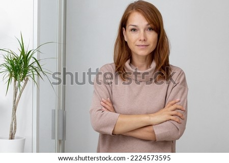 Waist up beautiful smiling middle aged woman holding crossed hands on breast looking at camera in light brown dress on white background Royalty-Free Stock Photo #2224573595