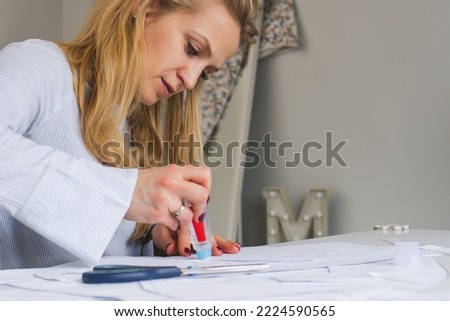 Woman tailor during work on sewing patterns. Seamstress glue together details of paper for dress