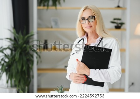 Female doctor wearing lab coat and stethoscope and holding clipboard in her hands while standing at hospital