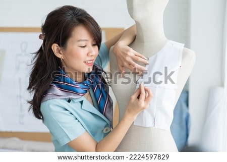 Asian female dressmaker using sketch paper measure measuring size of dress on the dummy mannequin in tailor shop. Fashion, dressmaking concept