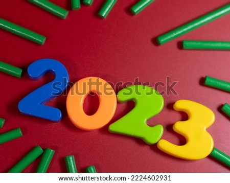 New Year's numbers on the table 2023 and decorative colorful sticks on a red background.
