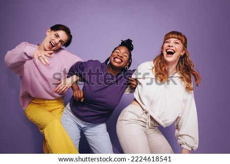 Vibrant multiethnic friends dancing and having fun in a studio. Group of happy female friends celebrating and having a good time against a purple background. Best friends making cheerful memories.