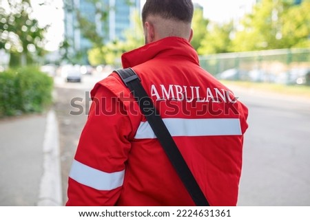 Ambulance staff member from the back with his emergency backpack , and vital signs monitor. Ambulance written on his back.