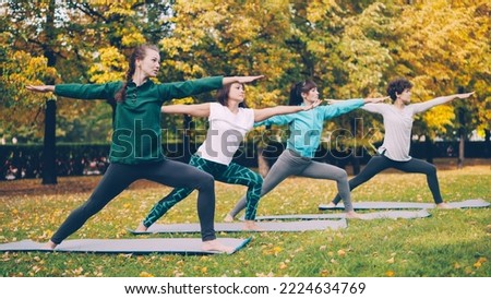 Yoga class is doing stretching exercises in park enjoying autumn nature, fresh air and physical activity. Well-being, recreation and sporty young people concept. Royalty-Free Stock Photo #2224634769