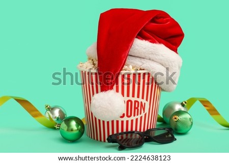 Bucket of popcorn with Santa hat, 3D glasses, ribbon and Christmas balls on green background