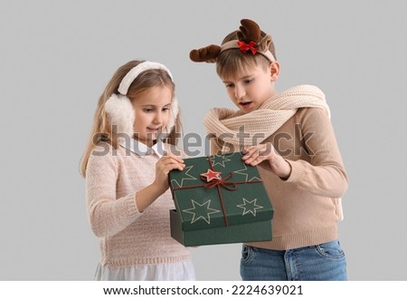 Little children opening Christmas gift on grey background
