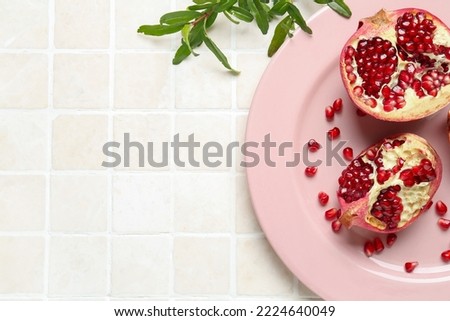 Plate with fresh pomegranates on light tile