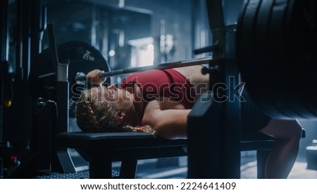 A Strong Woman Lifting Extremely Heavy Weights on a Barbell and Working Out. A Resolute Female Bodybuilder Training Alone in a Hardcore Dark Gym, Doing Bench Press Exercises Royalty-Free Stock Photo #2224641409