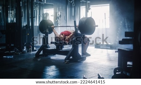 Professional Female Athlete Doing Bench Press Workout Using Barbell In a Grunge Hardcore Gym. An Inspiring Bodybuilder Training and Exercising with Heavy Weights In a Deserted Gym. Wide Shot Royalty-Free Stock Photo #2224641415