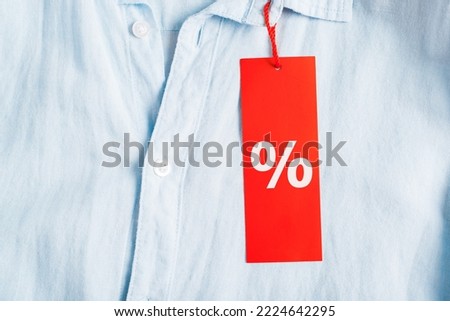 Sale, discount, black friday concept. Red tag with discount symbol Percent hanging on a light shirt, close-up.