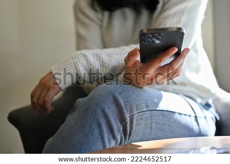 Attractive young Asian woman in casual clothes relaxes sitting in the coffee shop and using her mobile phone. cropped image