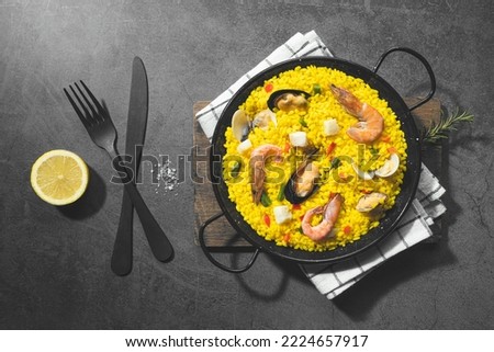 Seafood paella on traditional paella pan on dark concrete background. Top view.