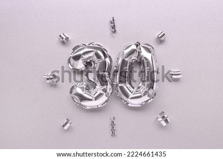 Number thirty inflatable balloons with ribbons confetti on a silver shiny background. Royalty-Free Stock Photo #2224661435