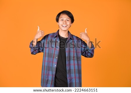 Potrait of smiling asian young man wearing shirt showing good gesture with thhumbs up isolated on yellow background