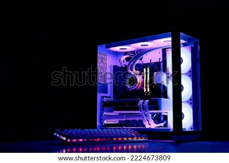 Gaming PC with rainbow LED light. Liquid cooled computer. Powerful PC in a glass case with keyboard. Gamer's workplace in a dark room, neon light