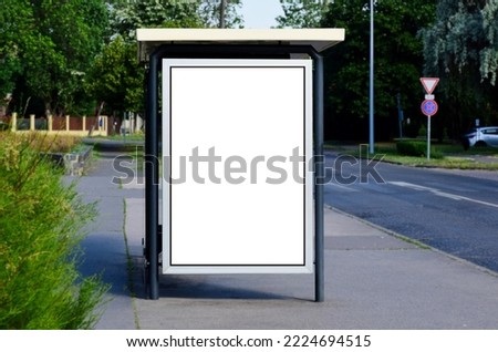 blank lightbox and glass bus shelter at busstop. green street setting. urban background. white ad poster and commercial space. display panel. empty vertical outdoor communication space. mockup base Royalty-Free Stock Photo #2224694515