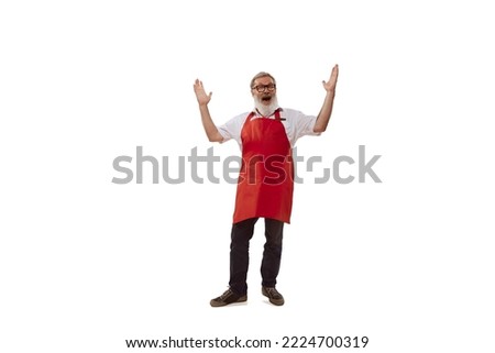 Portrait of senior man, cheerful salesman in red apron posing isolated over white background. Welcoming customers. Concept of shopping, hypermarket, supermarket, purchasing. Copy space for ad