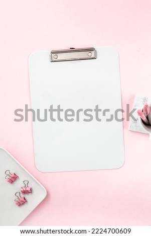 Feminine desktop flat lay of office workspace scene with white and silver stationery accessory items, including a mock-up of a blank white clipboard on a light pink pastel background