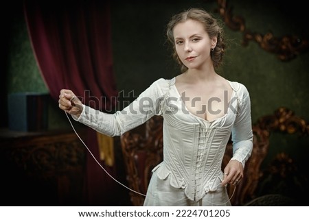 18th century Scottish clothing. A medieval noble woman is getting dressed in a Scottish costume of the 18th century in a vintage room. Scottish clothing of the 18th century.  Royalty-Free Stock Photo #2224701205