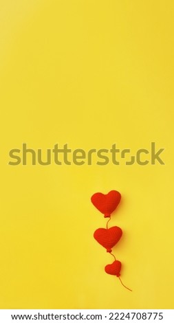 handmade three knitted red balloons heart shape in row on yellow background, copy space, vertical, 16:9