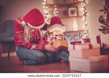 Mother and son indoors looking inside of gift box in Christmas eve. Concept of Christmastime and New Year.