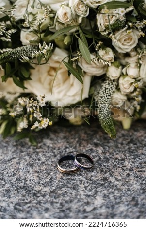 wedding engagement rings made of silver and dark stone lie on a granite surface against the background of the bride's bouquet