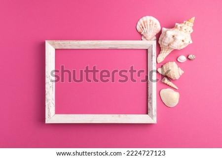 Top view of blank wooden picture frame with seashells decorations isolated on bright pink background. Mock up, copy space, flat lay.