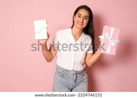 Portrait of an excited hispanic happy girl holding a gift box present on her head and looking at camera isolated over pink background