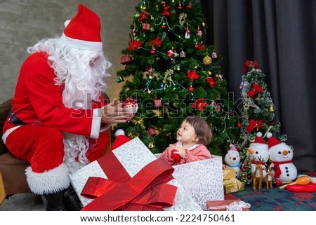 Caucasian baby is getting present from Santa claus at night by the fully decorated christmas tree for season celebration usage