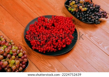 Fresh grapes.Red viburnum berry, cranberry. Still life on a wooden background.In a black plate.Fruit composition.Close-up. place for text