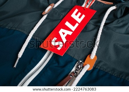 Advertising text Sale on a red tag attached to clothes, close-up. Black Friday, annual big sale with discounts concept.