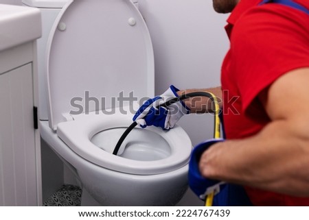 plumber unclogging blocked toilet with hydro jetting at home bathroom. sewer cleaning service Royalty-Free Stock Photo #2224767439