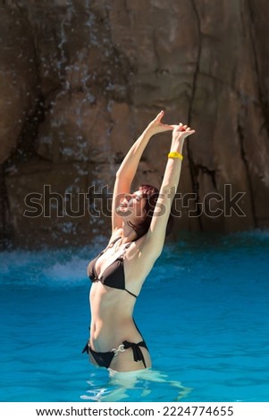 Beautiful woman bathes near rock with a waterfall.