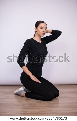full length woman sit and show poses on the floor in black tight fitting clothes and sneakers in the studio on a white background