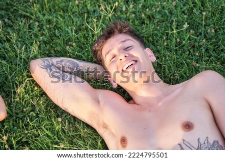 portrait of shirtless tattooed young man lying on the grass smiling