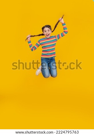 childhood studio shot of jumping teen braided girl. teen braided girl isolated on yellow background. Royalty-Free Stock Photo #2224795763