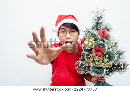 happy attractive Asian man in red Christmas theme clothes while holding christmas tree isolated over white. christmas concept man in red santa claus clothes.