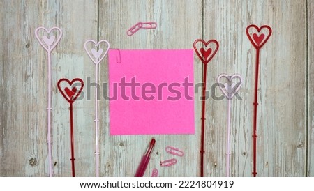 natural wood background with pink paper, pen, and heart decoration.