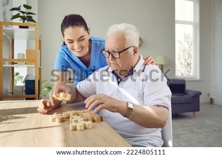 Nurse in retirement home helping old male patient with board game. Senior man with cognitive disorder sitting at table in geriatric clinic, playing games and thinking. Dementia, Alzheimers, care Royalty-Free Stock Photo #2224805111