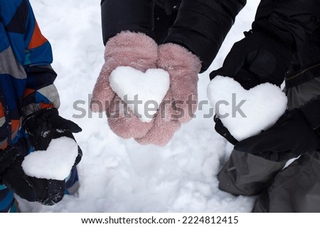 hands of two adults and a child in mittens hold 3 hearts made of snow. Friendly family. Snow games. Love winter, fun winter seasonal activities. soft focus