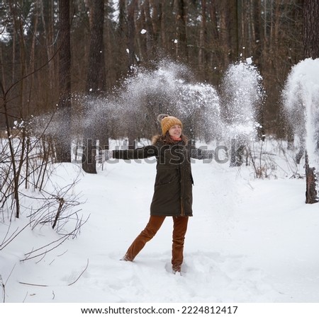 young woman in warm clothes having fun with fresh snow in winter in the park. She throws snow with her hands, smiles. I love winter, merry Christmas holidays. soft focus