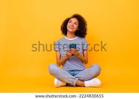 Full body photo of cheerful nice lady sit floor hold telephone look empty space isolated on yellow color background