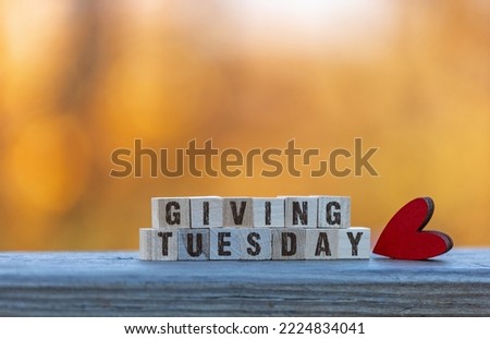 Giving Tuesday text on wood blocks with red heart golden leaves bokeh background Royalty-Free Stock Photo #2224834041
