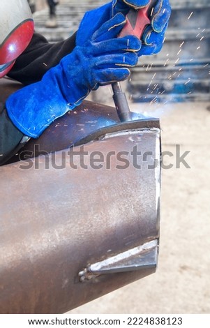 A professional welder in a protective suit and mask produces the connection of pipes with the help of a welding machine on the construction site. Royalty-Free Stock Photo #2224838123