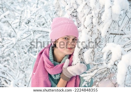 A young woman on the background of a beautiful plant in the snow. A young lady blows a kiss during a snowfall. Great mood, joy, fun.